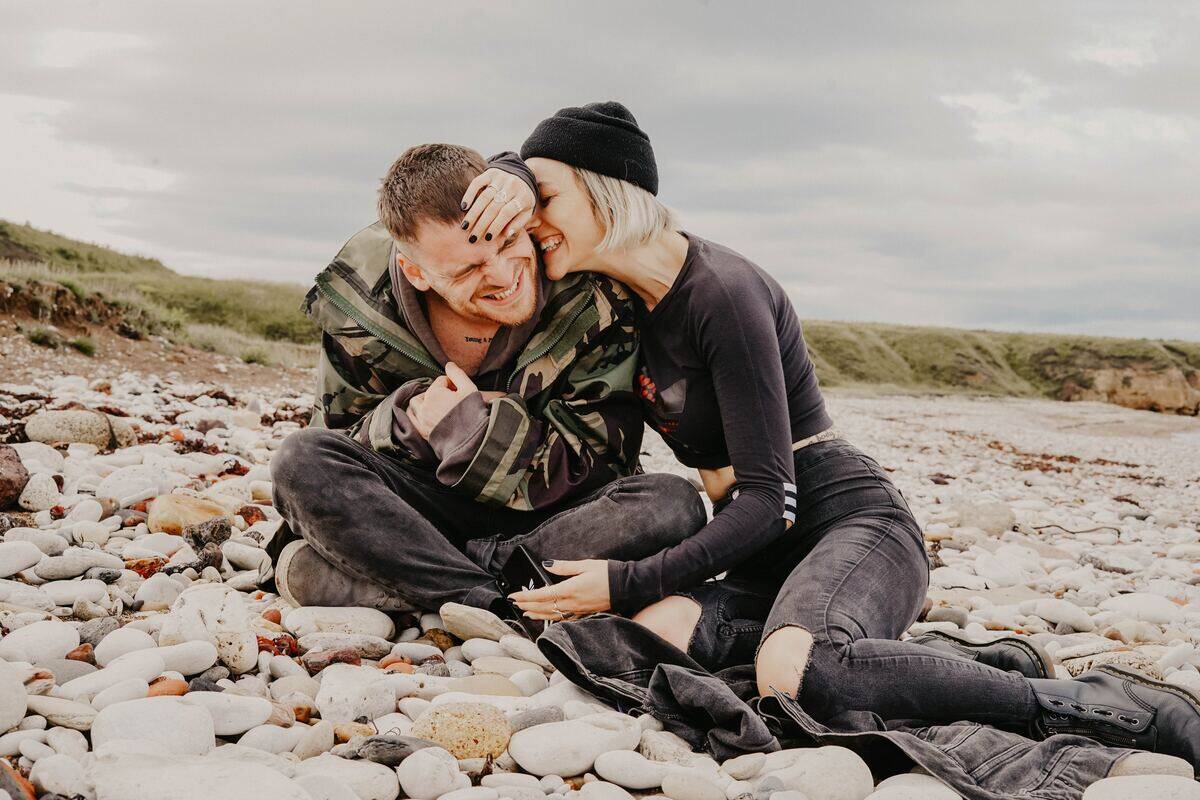 woman laughing while pressing up to man while they sit on rocks