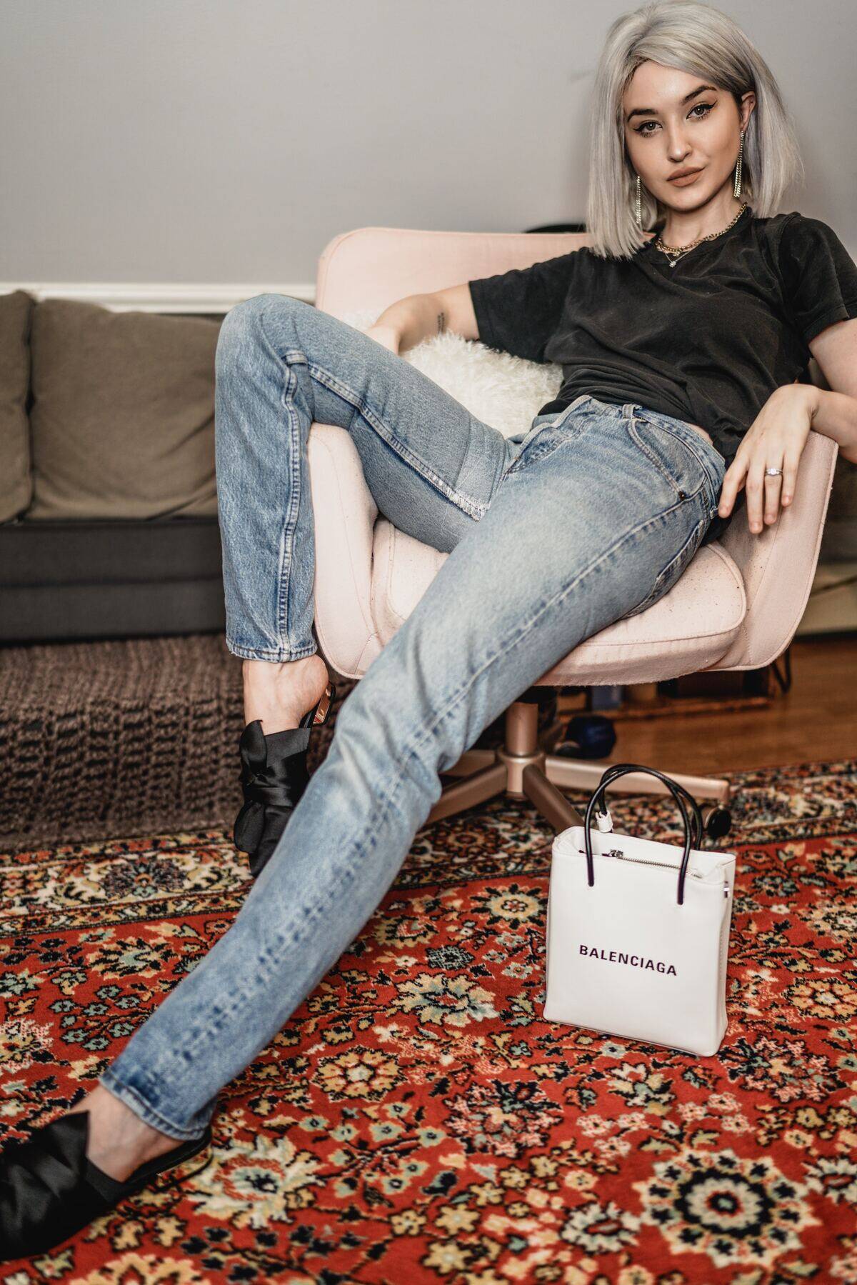 woman lounging in char next to Balenciaga bag