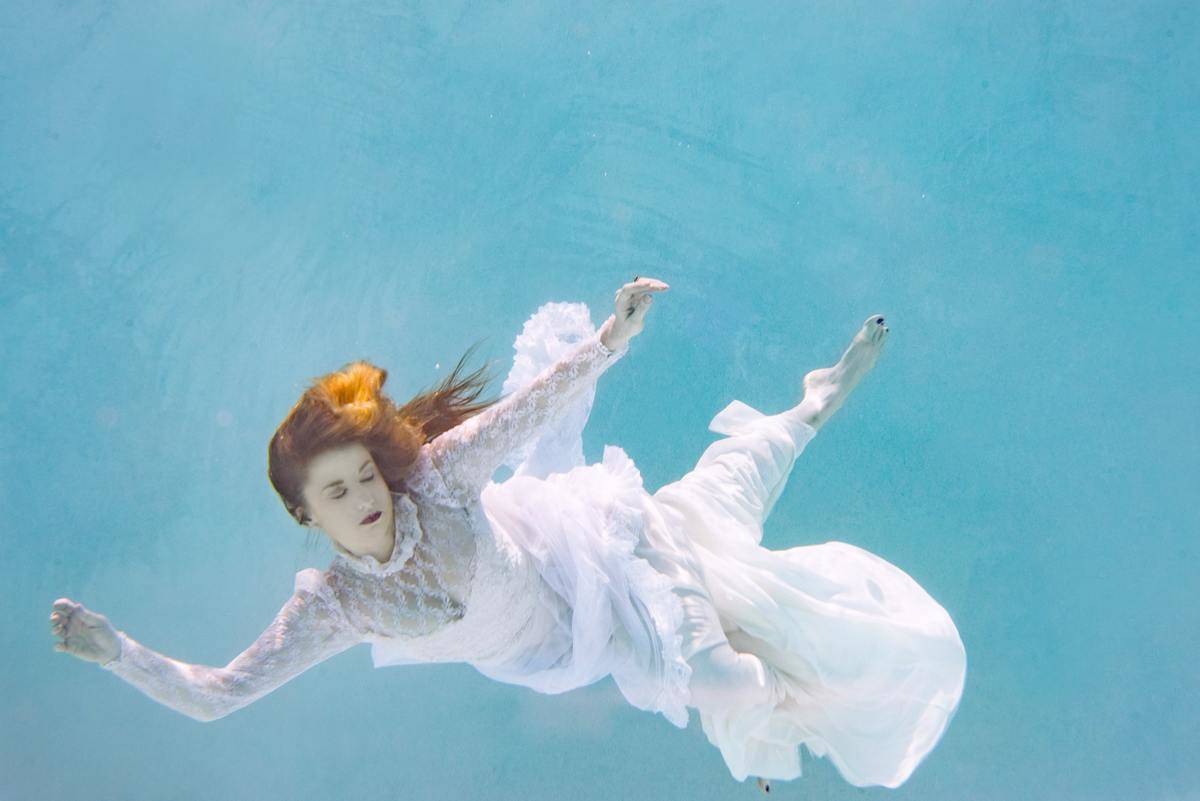a woman swimming underwater in a white dress