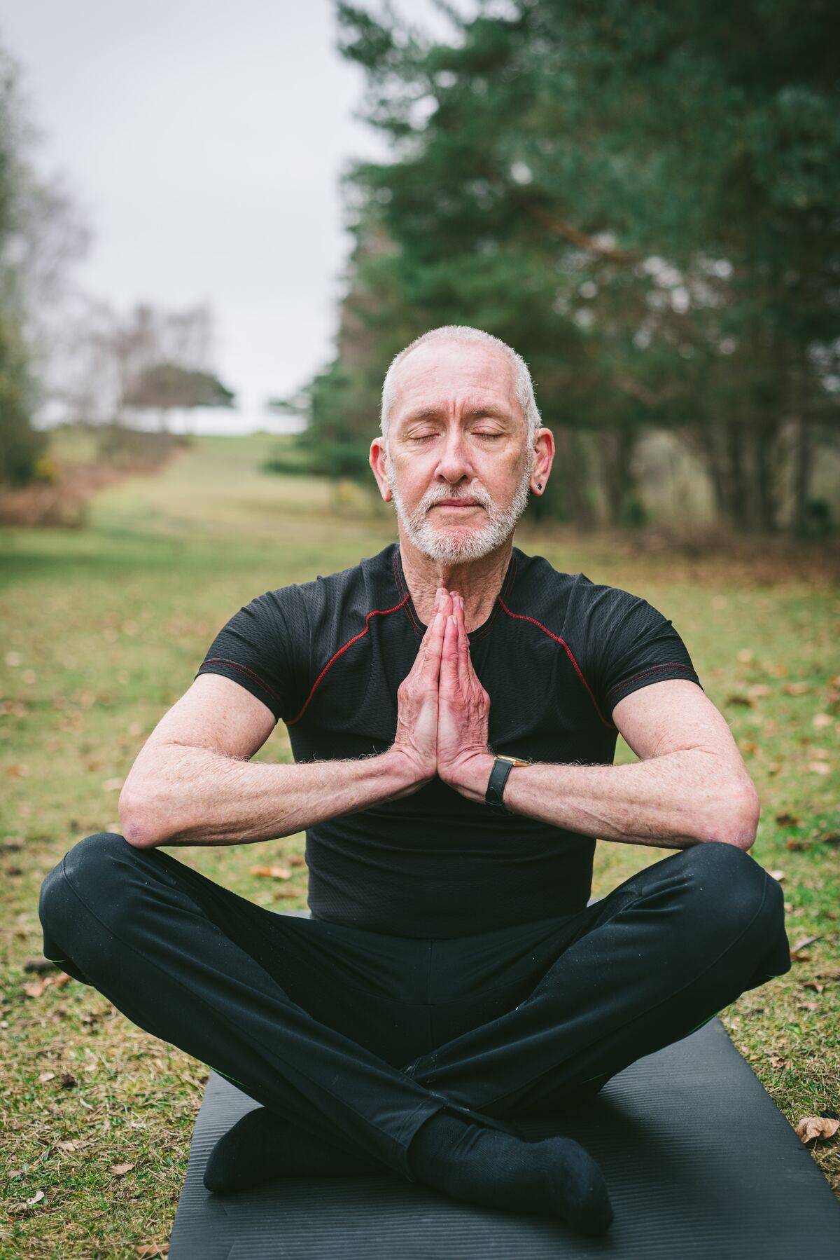 older man meditating on yoga mat in park
