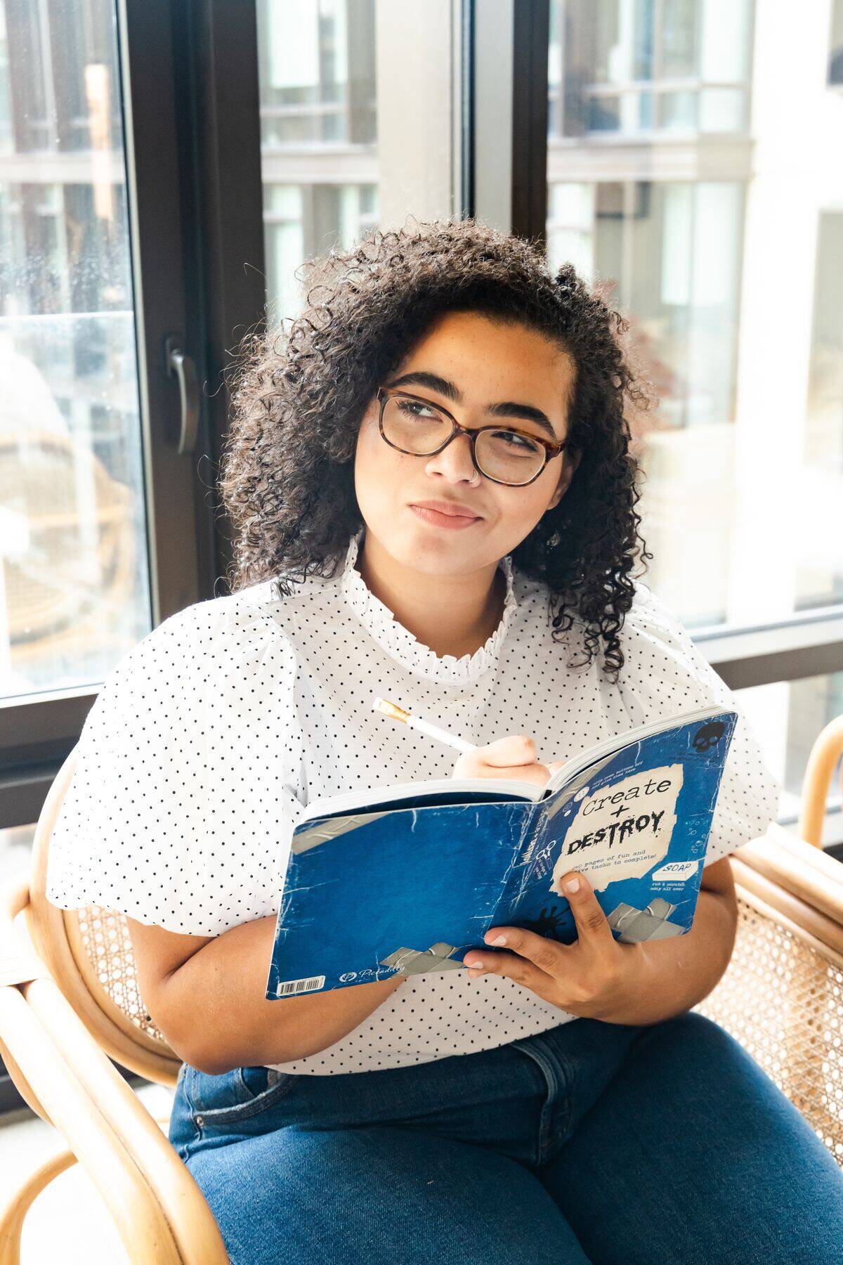 woman in glasses thinking while writing in notebook