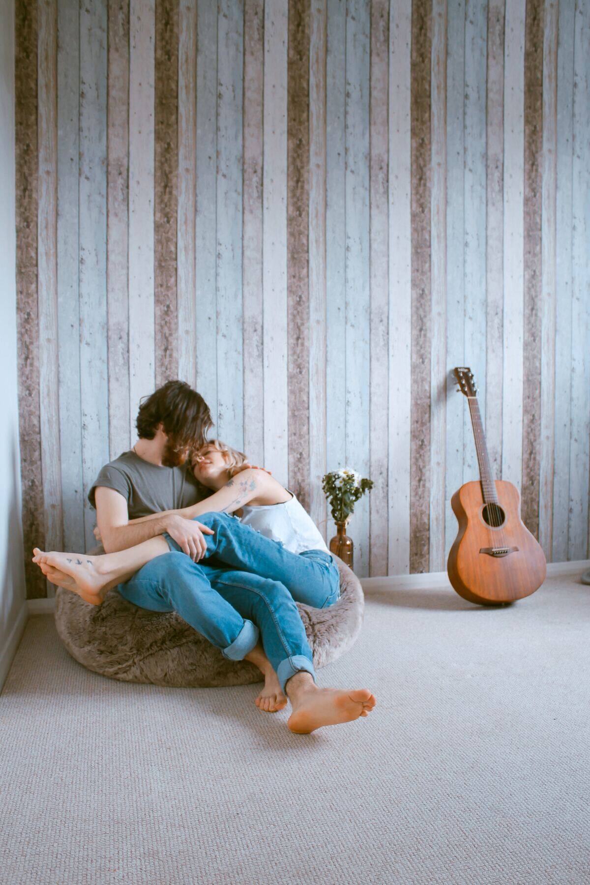 couple cuddling in bean bag chair next to guitar in otherwise empty room