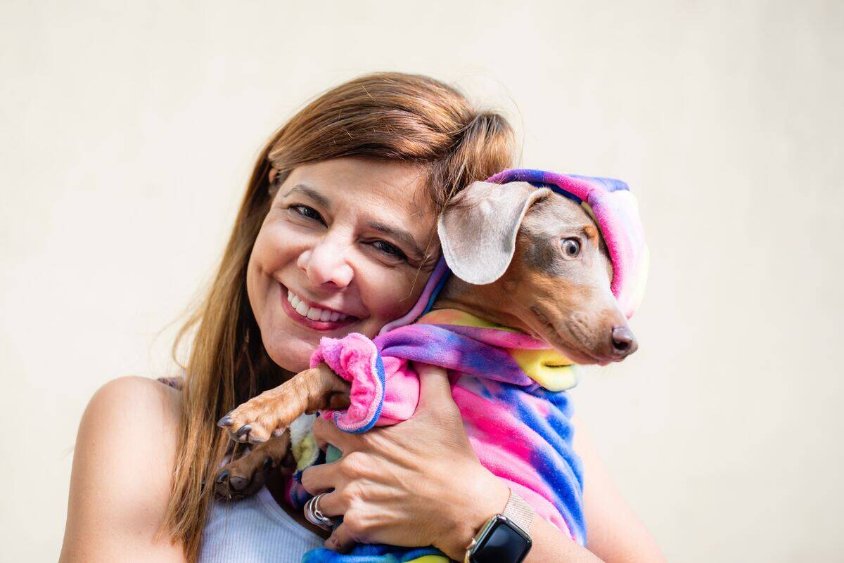 woman holding a dachshund dog in a colorful outfit