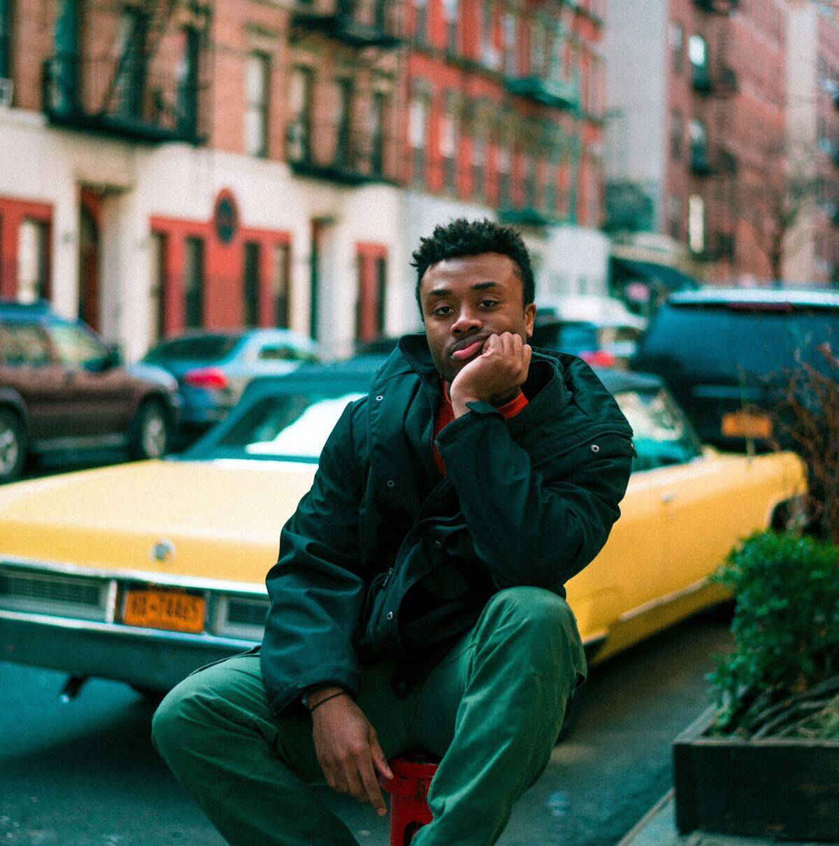 man sitting with face in hand behind yellow car
