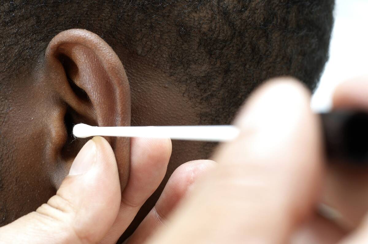 GP using cotton bud to clean ear canal of young male patient
