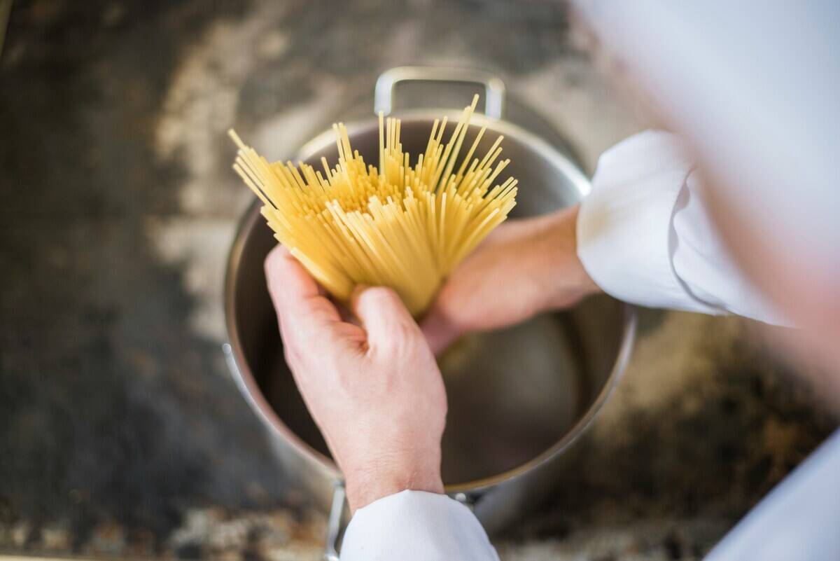 spaghetti being dumped into a pot of boiling water