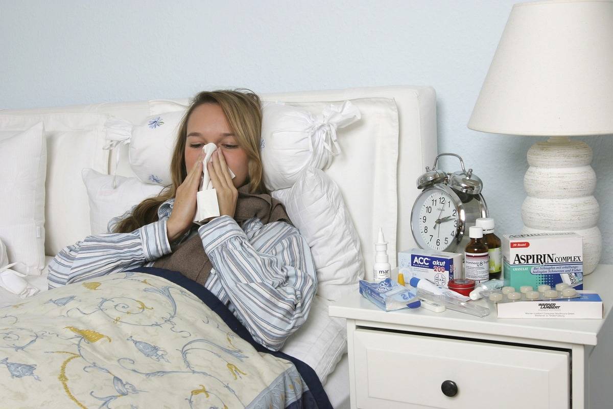 An ill woman blows her nose while laying in bed.
