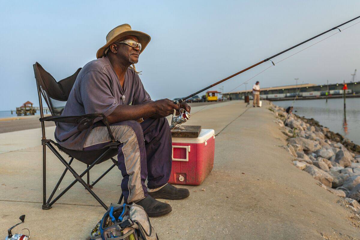 Black man with sunglasses fishing on the jetty at the Gulfport Municipal Marina in Gulfport, Mississippi