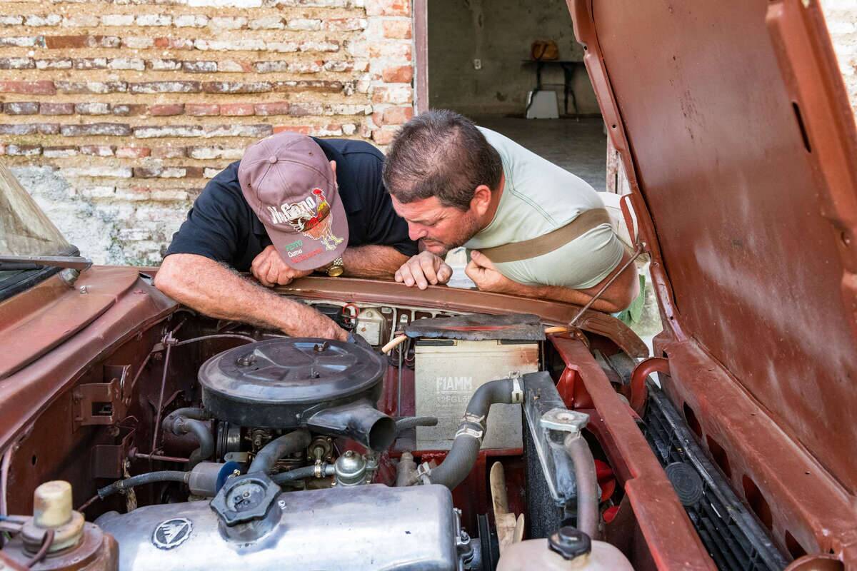 Two Cuban men repairing a car in the city street. It is a...