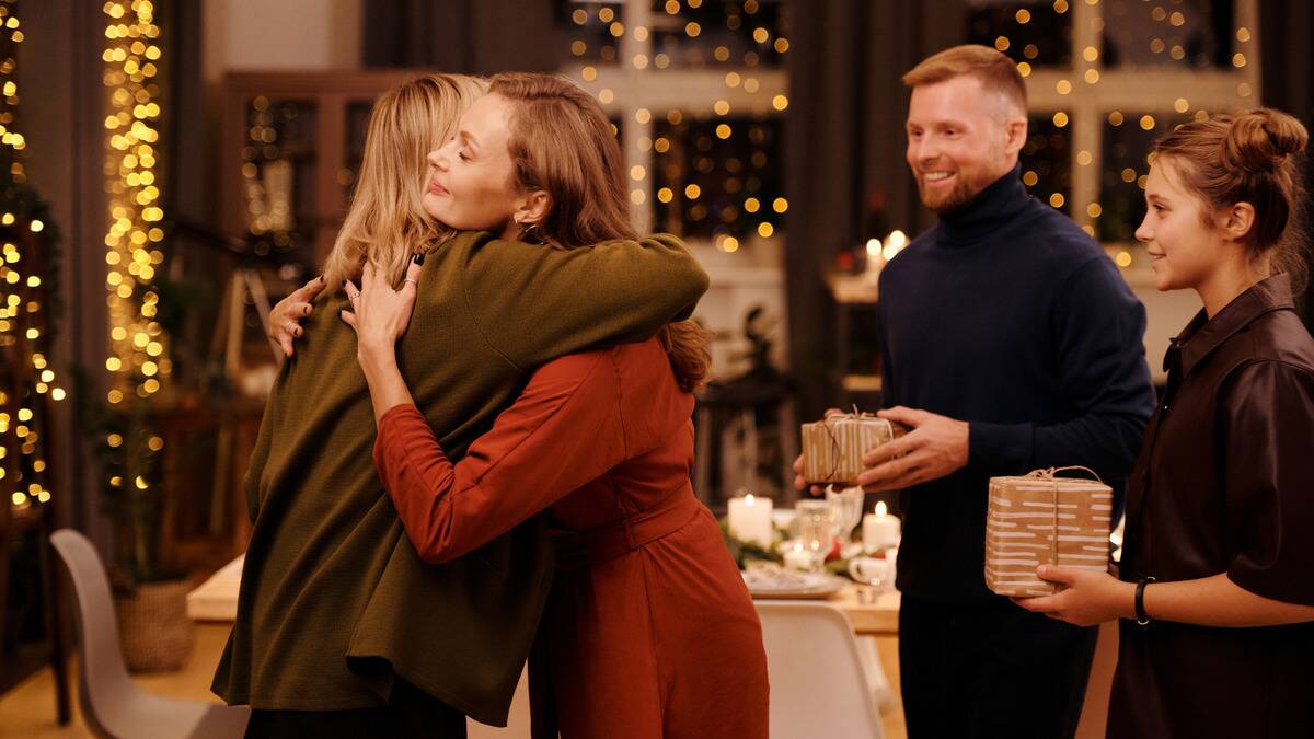 Two woman hugging at a holiday reunion, two people off to the side smiling as they watch.
