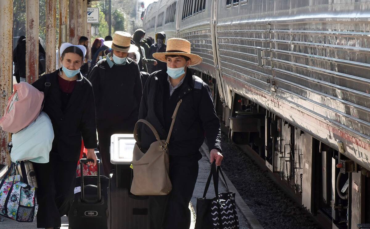 Amish rail passengers wearing face masks walk on the...