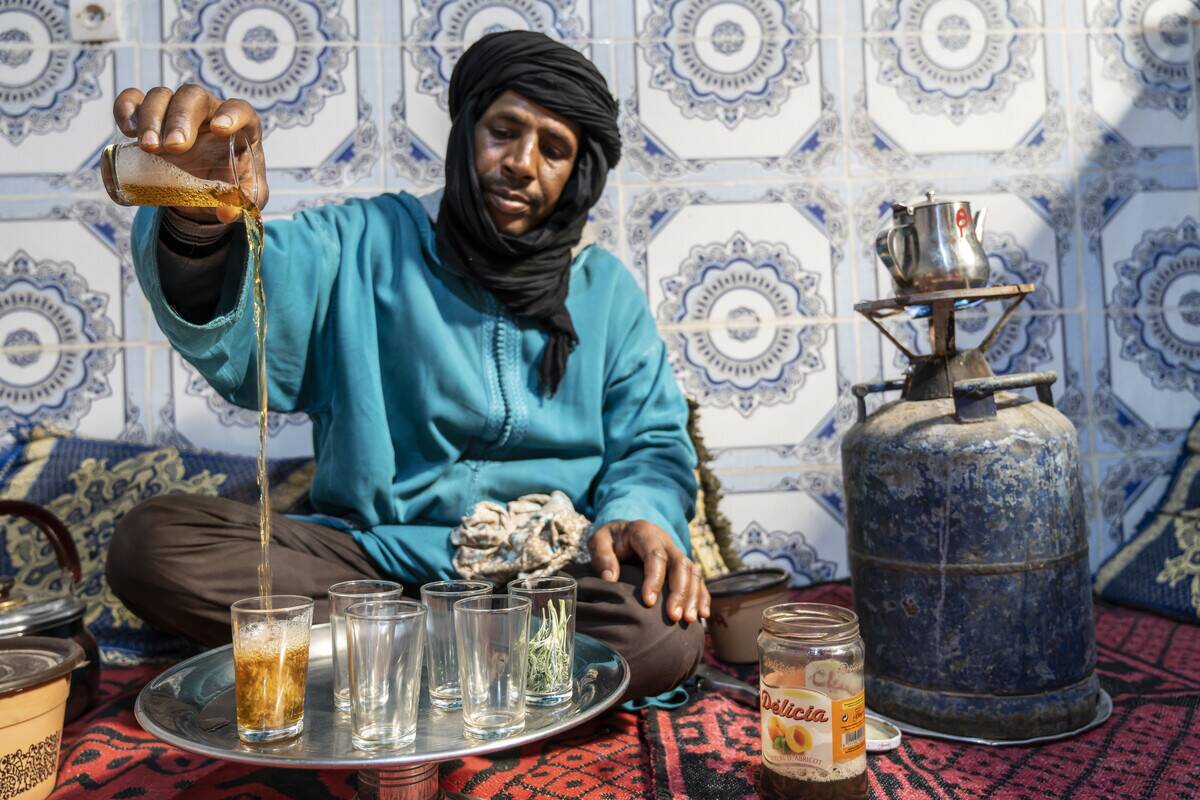 Berber man dressed in djellaba and black turban serving tea...