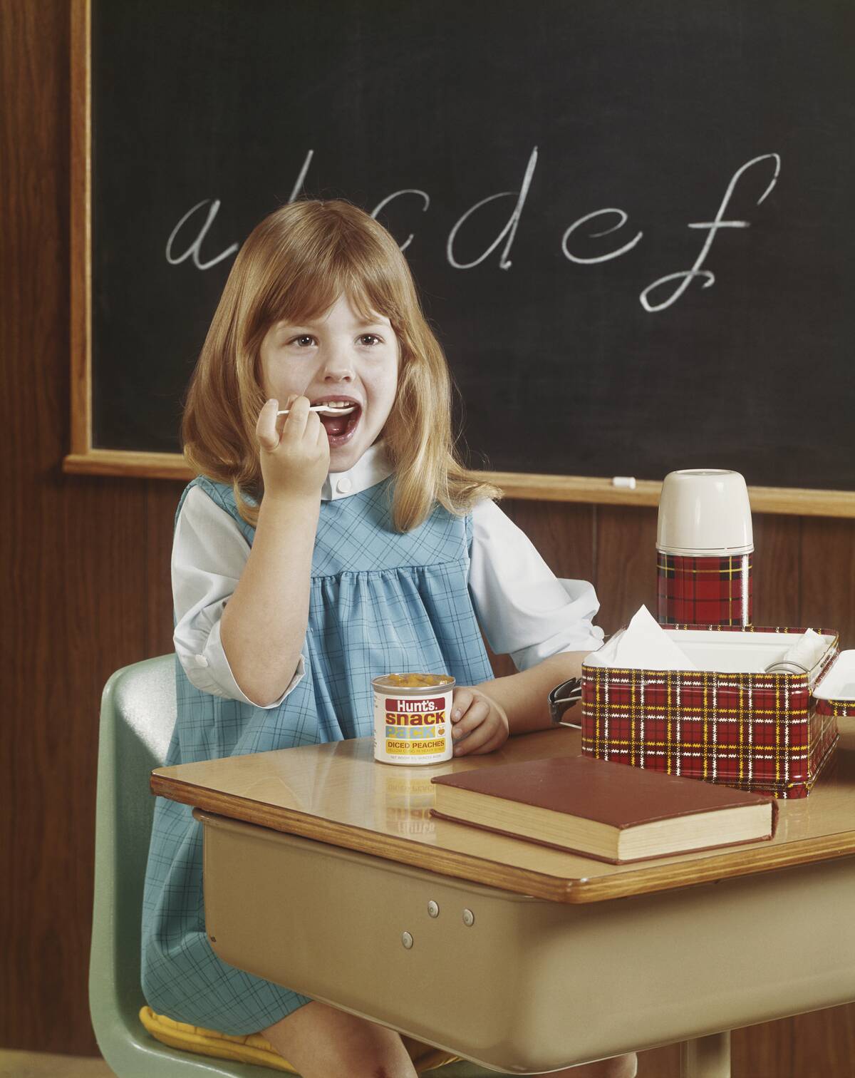 Girl eating canned food sitting beside blackboard