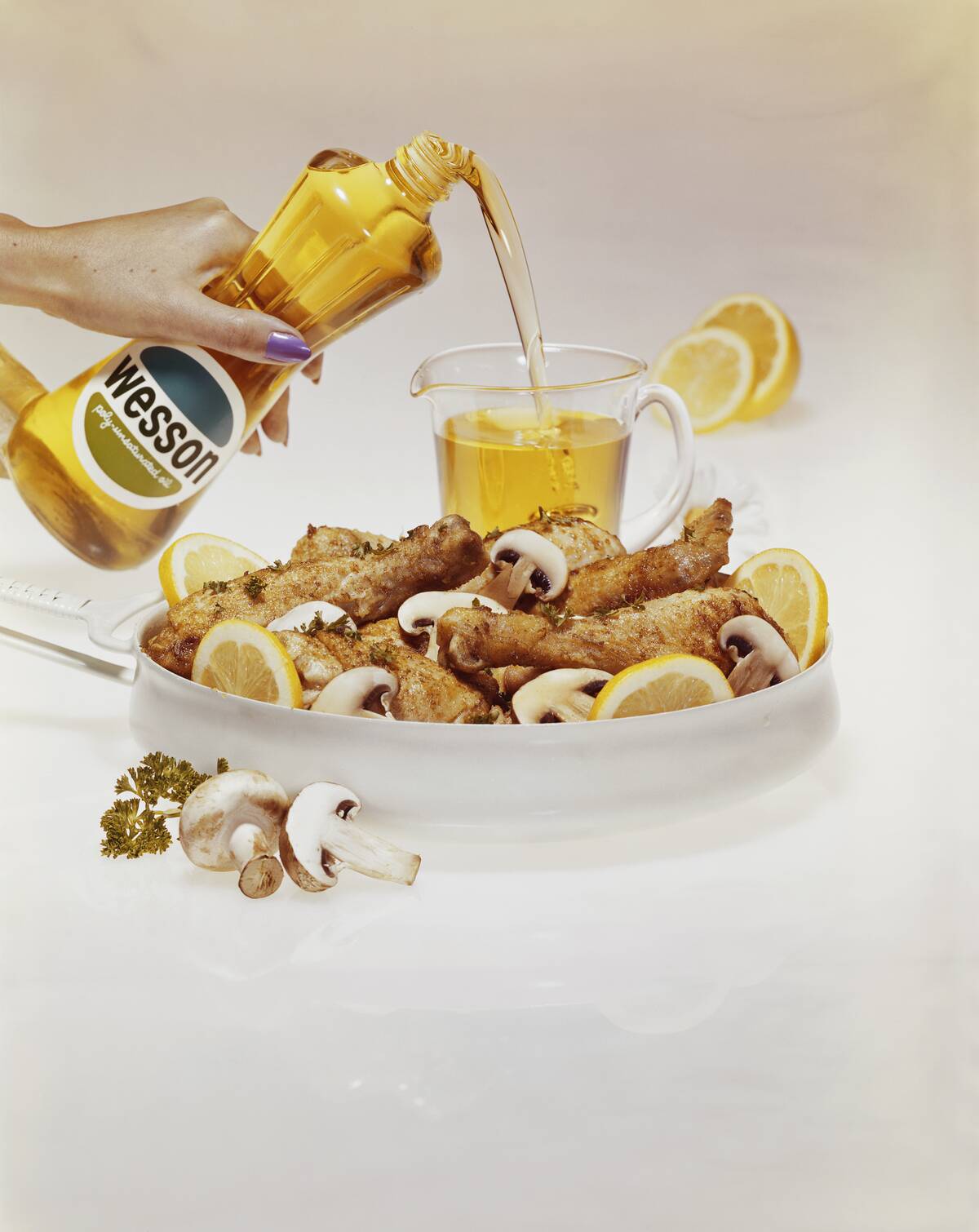 Woman pouring vegetable oil into glass beside plate of chicken and edible mushroom