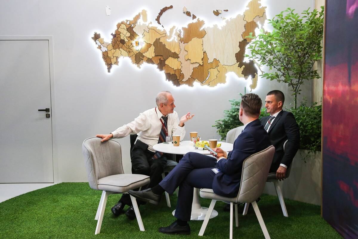 Forum visitors sit at a table and talk against the backdrop...