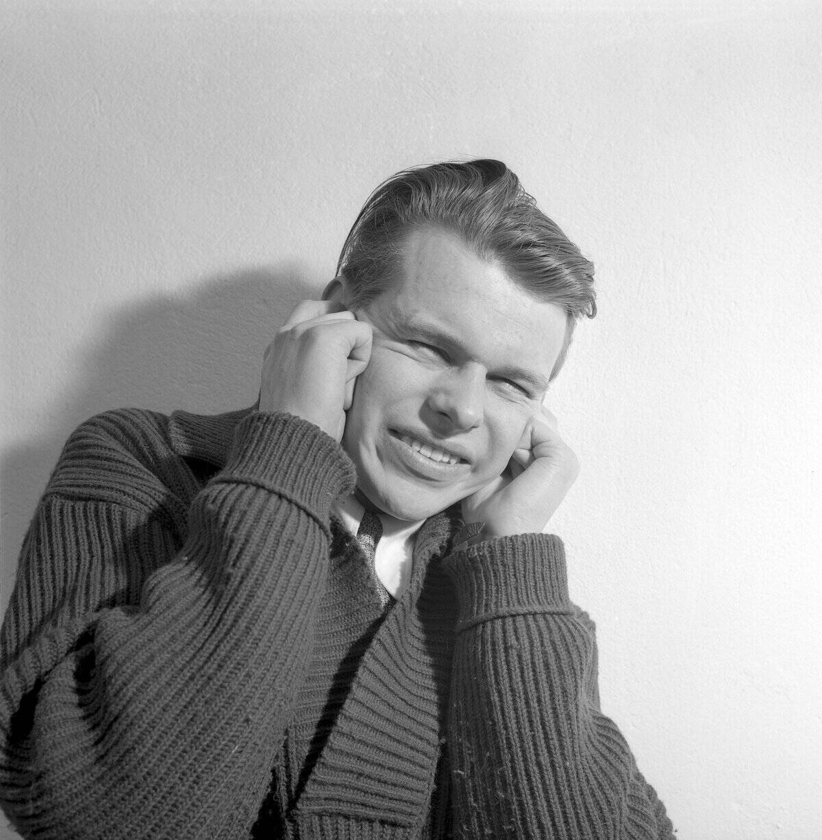 In the 1950s. A young man holds his hands over his ears and has a facial expression that indicates tha...