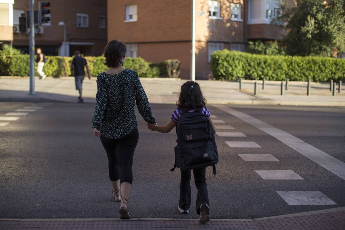 A girl with her backpack and holding her mother's hand...