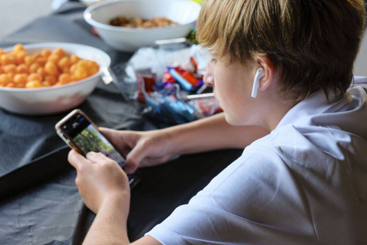 Preteen boy concentrating on smartphone with ear buds and bowls of snacks