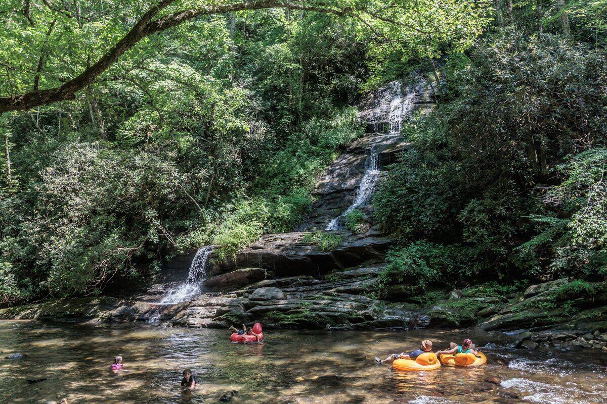 Visitors swimming and floating on inflatables at the base of Tom Branch Falls along Deep Creek in the Smoky Mountains near Bryson City, North Carolina, USA