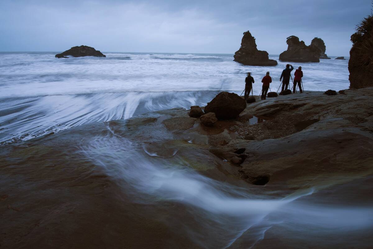 Photo workshop group at sunset on overcast day on the shore of Tasman Sea. New Zealand