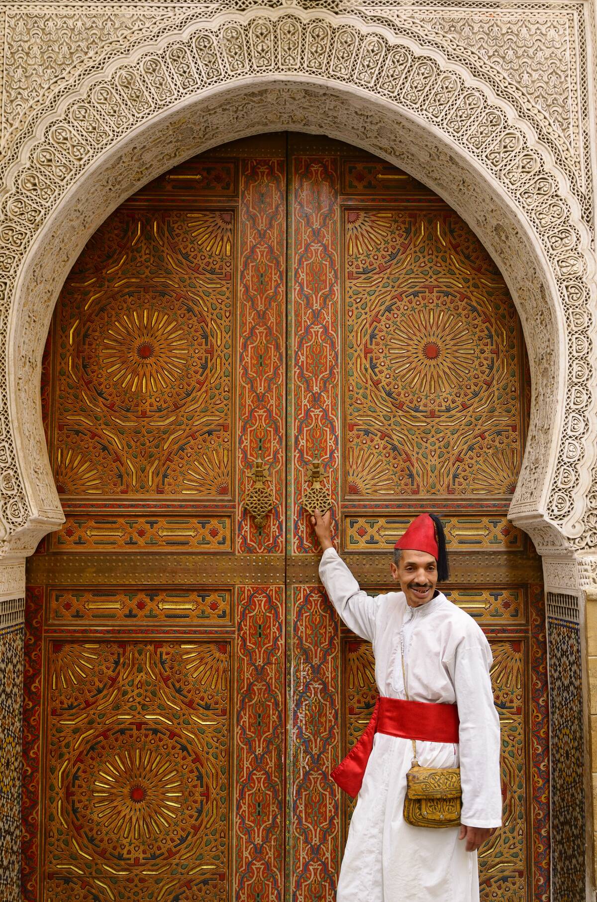 Man in white robe and red cap and sash at door of Mosque