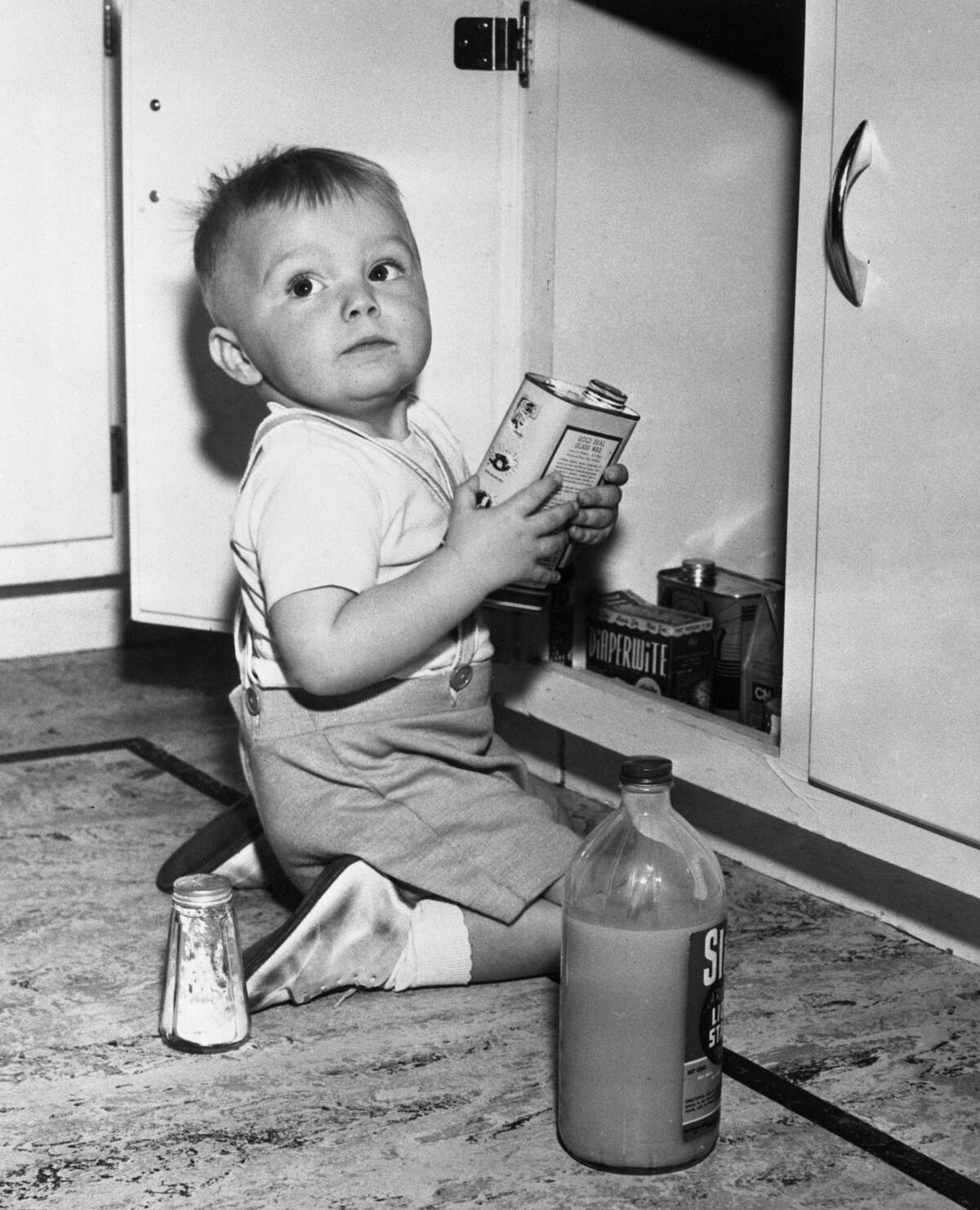 Boy (2-3) kneeling on floor in front of cupboard with bottles