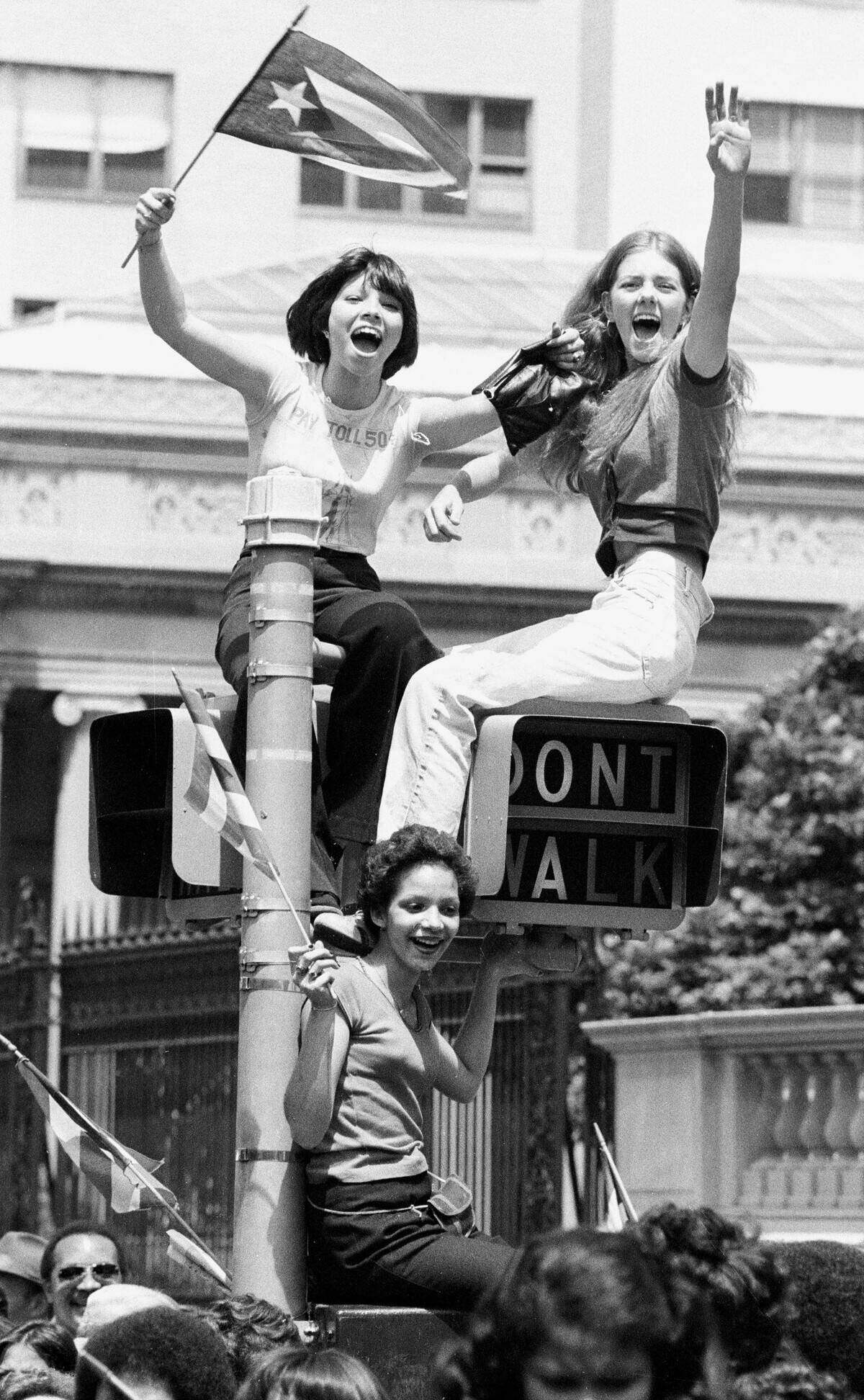 Three senoritas use traffic signal as perch as they cheer ma