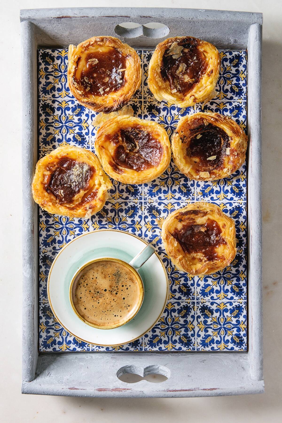 Traditional Portuguese egg tart dessert Pasteis Pastel de nata in classic tile tray with cup of black coffee. Flat lay. space.